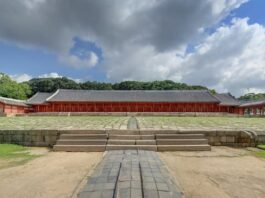 Wide front-facing photograph of Jeongjeon Hall at Jongmyo Shrine in Seoul with its broad stone courtyard and central ceremonial path